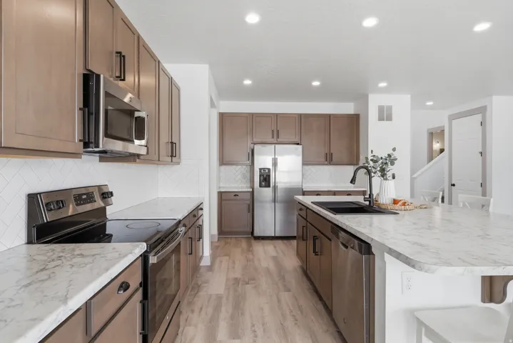 Open-concept kitchen with wood-finish flooring, light-toned cabinetry, stainless steel appliances, white patterned backsplash, and a central island with a sink