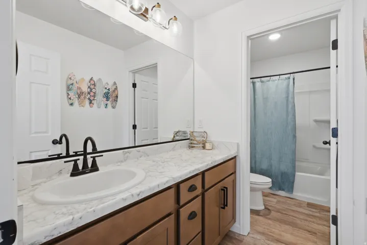 Spa-inspired primary bathroom featuring a wood-finish vanity with dual sinks, marble countertop, and matte black hardware