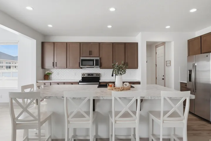 Central island with a light-toned countertop, wood-finish cabinetry, stainless steel appliances, and a white subway tile backsplash