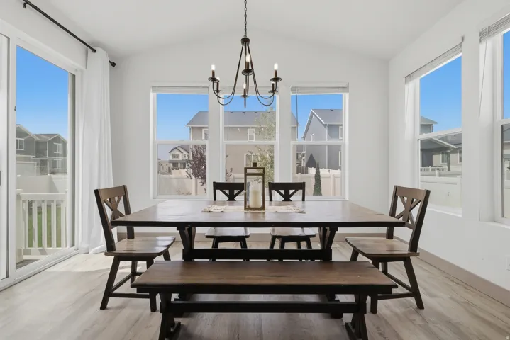 Vaulted ceiling, wood-finish flooring, multiple windows, sliding glass door, and a decorative chandelier