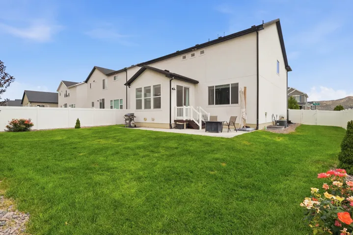 Expansive backyard featuring a large green lawn, concrete patio, and white privacy fencing