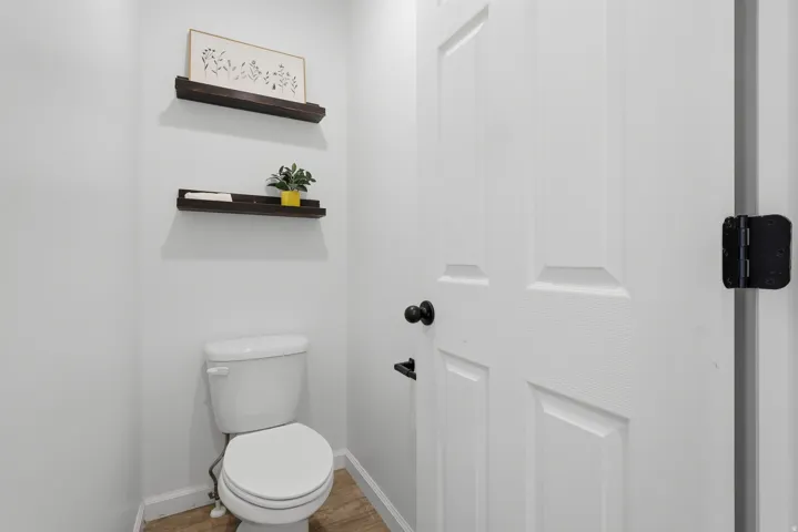White paneled door with black hardware, wood-finish flooring, and wall-mounted shelving