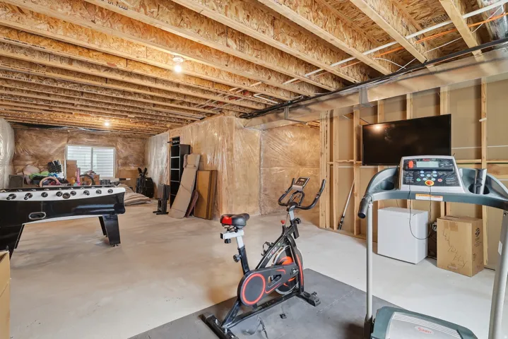 Unfinished basement featuring exposed joists, concrete flooring, and an egress window