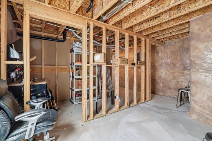 Unfinished basement featuring exposed wood framing, concrete flooring, and an open ceiling with exposed ducts