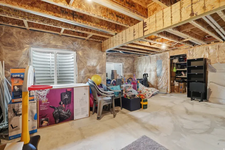 Unfinished basement with exposed ceiling joists, concrete flooring, two egress windows, and a built-in storage alcove