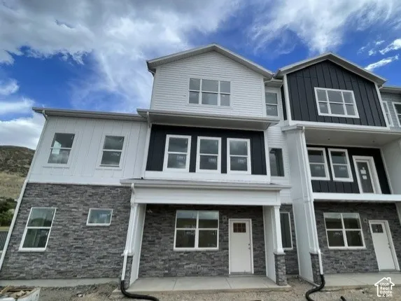 Multi-level facade featuring vertical and horizontal siding, stone veneer accents, multiple window styles, and column-supported entryways
