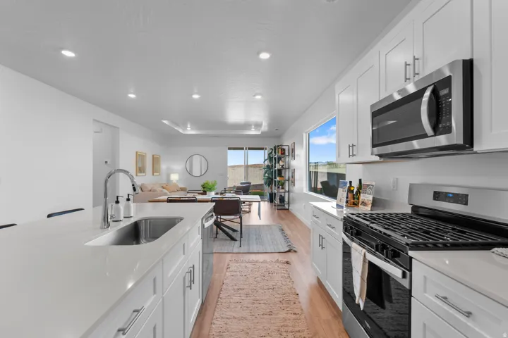 Stainless steel appliances, recessed lighting, wood-finish flooring, white cabinetry, and a large kitchen island with an undermount sink