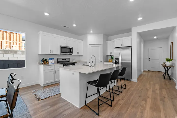 Modern kitchen featuring white cabinetry, stainless steel appliances, a center island with seating, and wood-finish flooring