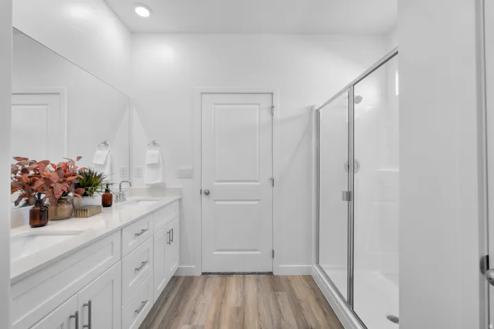 Dual vanity with undermount sinks, wood-finish flooring, recessed lighting, and a glass-enclosed shower