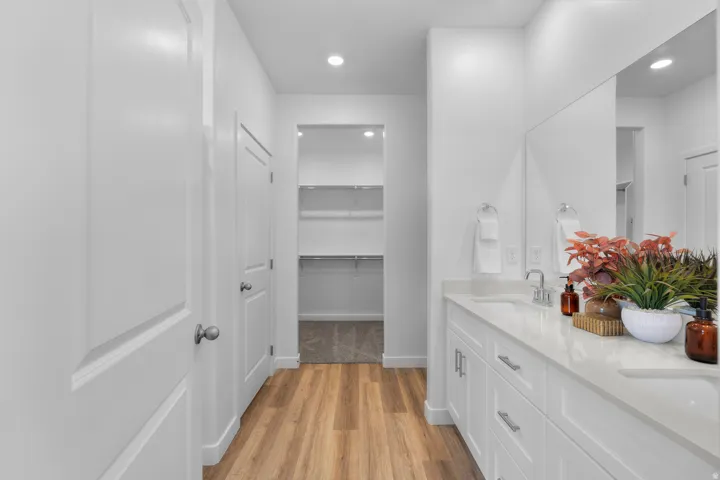 Double vanity with integrated sinks, wood-finish flooring, recessed lighting, and a walk-in closet with built-in shelving