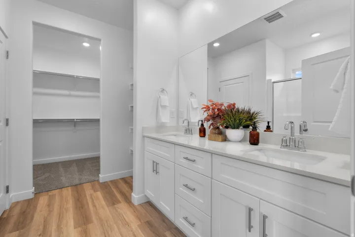 Double vanity with white cabinetry and integrated sinks, wood-finish flooring, large wall-mounted mirror, and recessed lighting