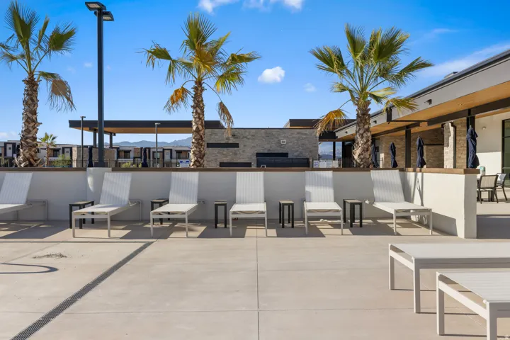 Expansive hardscaping with multiple lounge chairs, surrounded by palm trees and architectural lighting, featuring an integrated stone-clad structure with a covered patio area