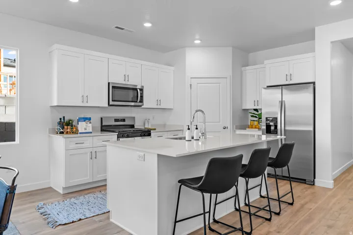 Kitchen featuring white cabinetry, stainless steel appliances, a center island with seating, pendant lighting, and wood-finish flooring