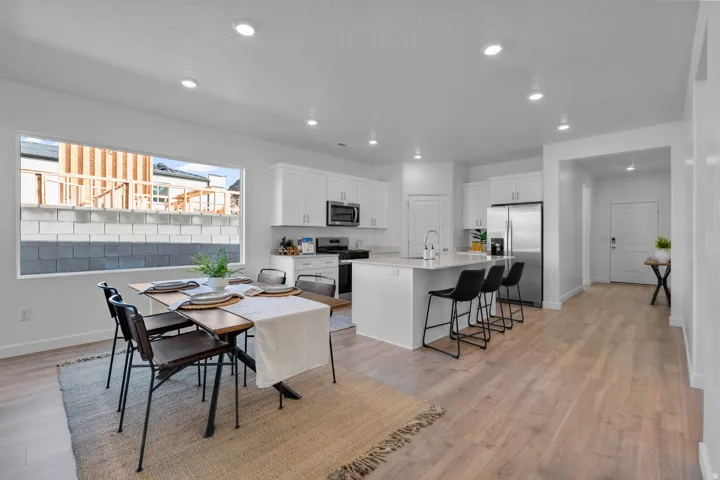 Open-concept living space with wood-finish flooring, recessed lighting, and a white kitchen featuring stainless steel appliances