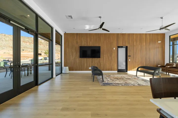 Wood-finish flooring, full-height wood paneling, dual ceiling fans, and expansive glass doors opening to an outdoor patio