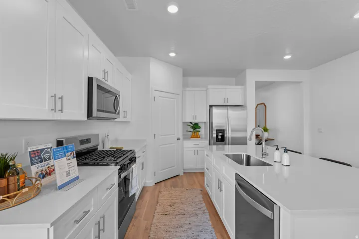 Modern kitchen featuring white shaker cabinetry, stainless steel appliances, light-toned countertops, a center island with an undermount sink, and wood-finish flooring