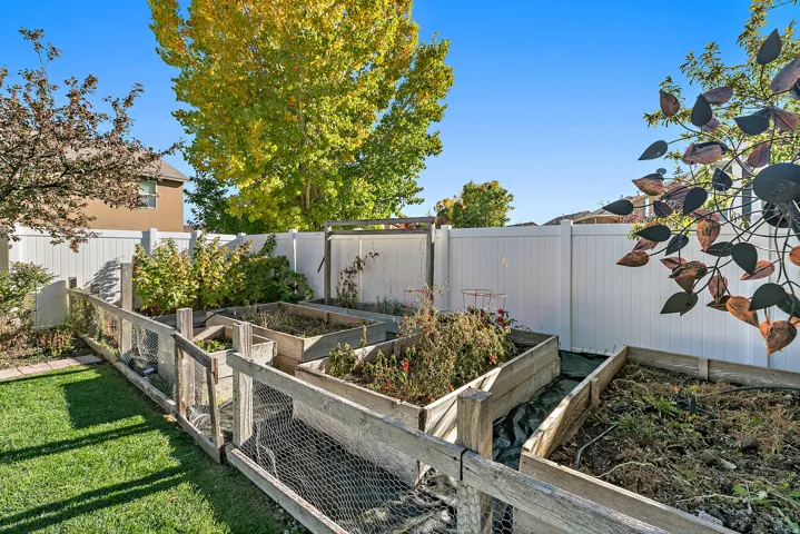 Fenced backyard featuring multiple raised garden beds and a manicured lawn