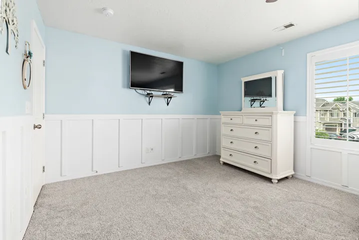 Board and batten wainscoting, light blue wall paint, window with white louvered blinds, and gray carpet