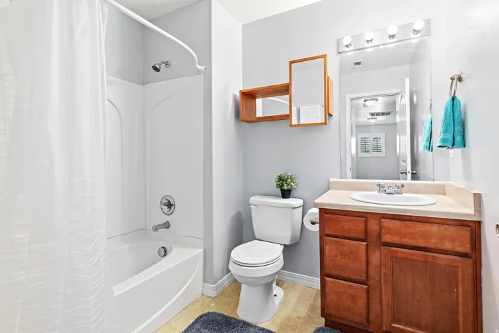 Bathroom featuring a white bathtub, chrome shower fixtures, a vanity with a light-toned countertop, and a wood-finish cabinet