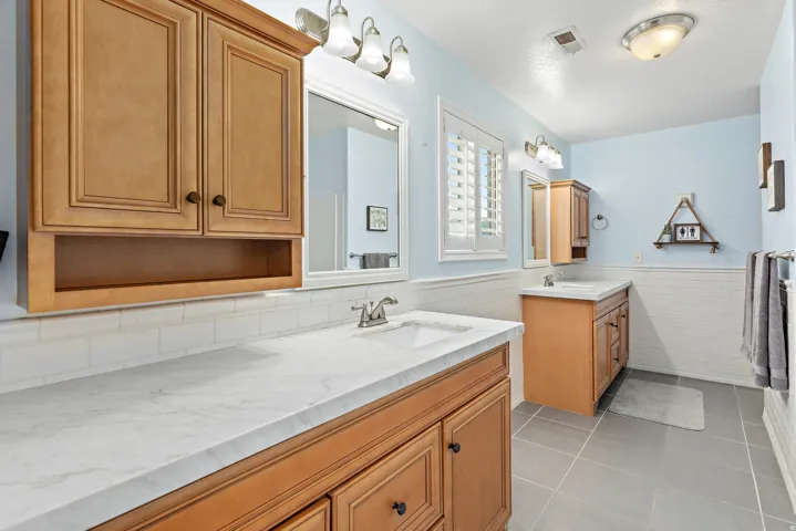 Dual wood-finish vanities with white countertops, integrated sinks, and chrome faucets