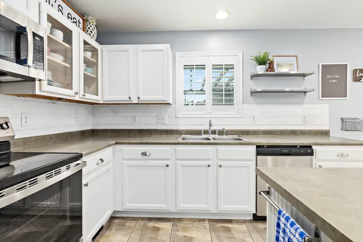 White cabinetry with brushed nickel hardware, stainless steel appliances, wood-finish flooring, solid surface countertops, and a white subway tile backsplash
