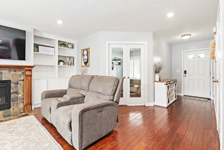 Hardwood-finish flooring, built-in shelving, fireplace with stone and wood surround, white interior doors, and recessed lighting