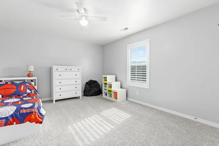 Carpeted room with a ceiling fan, a window featuring plantation shutters, and light gray painted walls