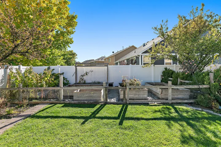 Fenced backyard featuring a manicured lawn, brick paver path, and multiple raised garden beds