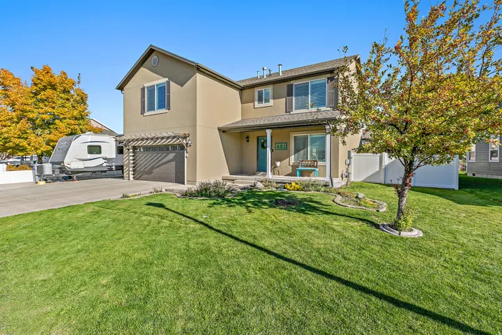 Two-story stucco exterior, attached garage with pergola detail, covered front porch, and expansive front lawn