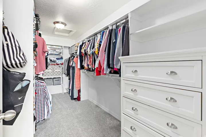 Built-in drawer storage, recessed lighting, white shelving, clothing rods, and light gray carpeting