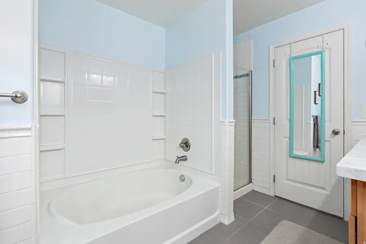 White tiled bathtub with an integrated shower, featuring a built-in shelf