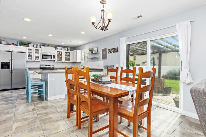 Open-concept kitchen and dining area featuring tile flooring, white cabinetry, stainless steel appliances, and a sliding glass door to the exterior