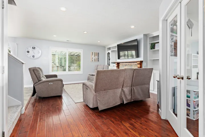 Hardwood-finish flooring, recessed lighting, built-in shelving, fireplace with stone surround, and French doors