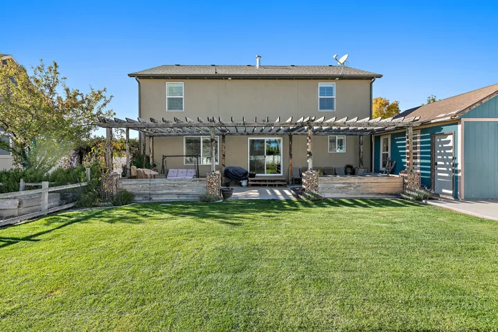 Expansive green lawn with a pergola-covered patio, featuring a sliding glass door and an additional built-in deck area
