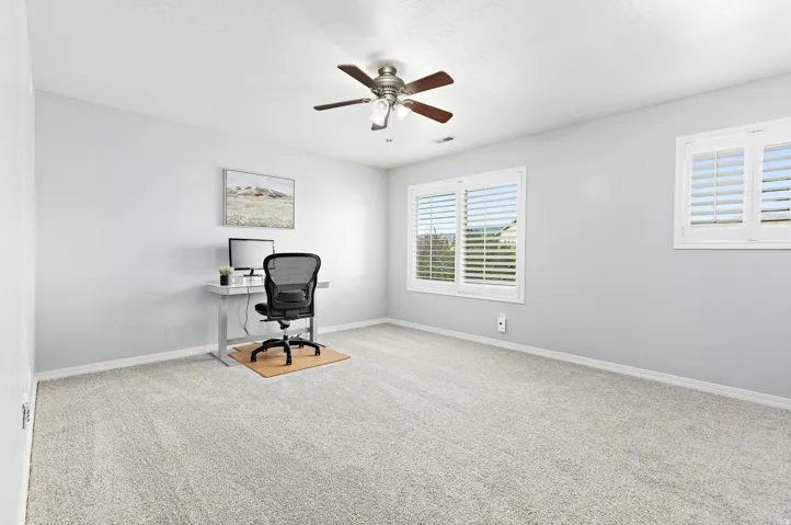 Plush carpeting, two windows with white plantation shutters, a ceiling fan with integrated lighting, and light grey wall paint