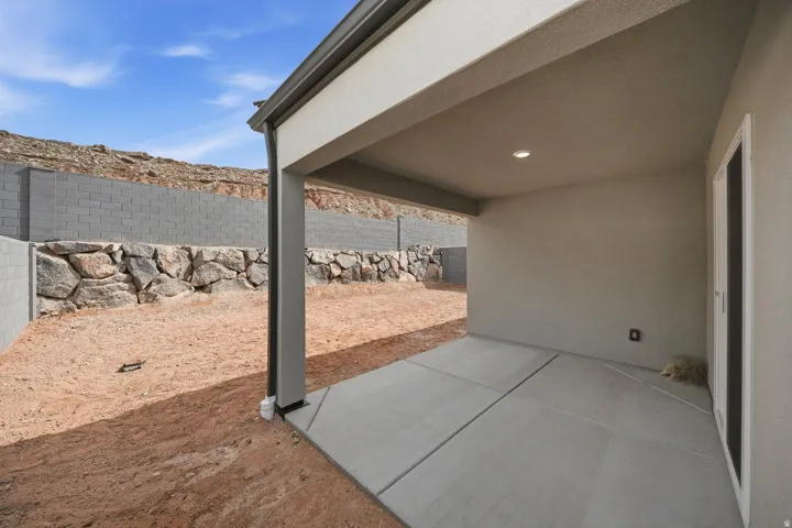 Covered patio with concrete flooring, recessed lighting, and a rock retention wall with a block wall surround
