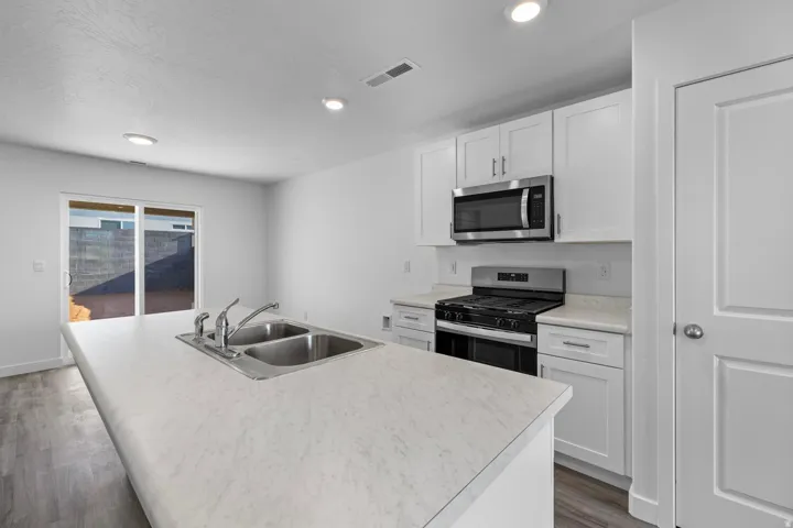 Kitchen featuring white shaker cabinetry, stainless steel appliances, a center island with a dual basin sink, and light-toned countertops