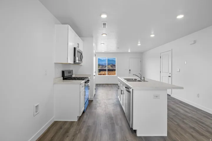 Kitchen featuring white cabinetry, stainless steel appliances, an island with an integrated sink, and wood-finish flooring