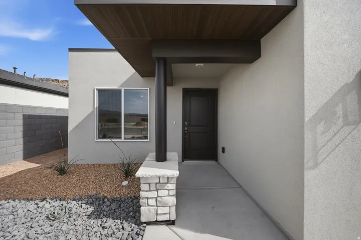 Modern stucco exterior with a dark wood-finish soffit, a solid wood entry door, and a stone-clad column base