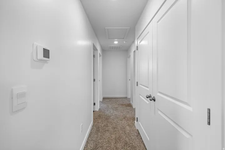 Recessed lighting illuminates the hallway, featuring light-toned carpet flooring and panel doors with dark hardware