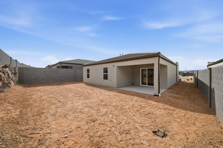 Expansive backyard featuring a covered patio, concrete block perimeter fencing, and a stucco exterior with a tile roof