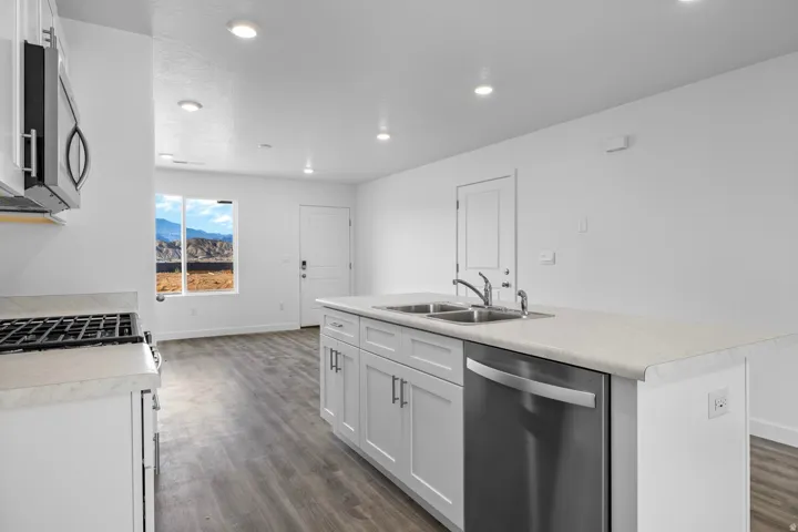 Kitchen featuring an island with dual sinks, white cabinetry, stainless steel dishwasher, and stone-finish countertops