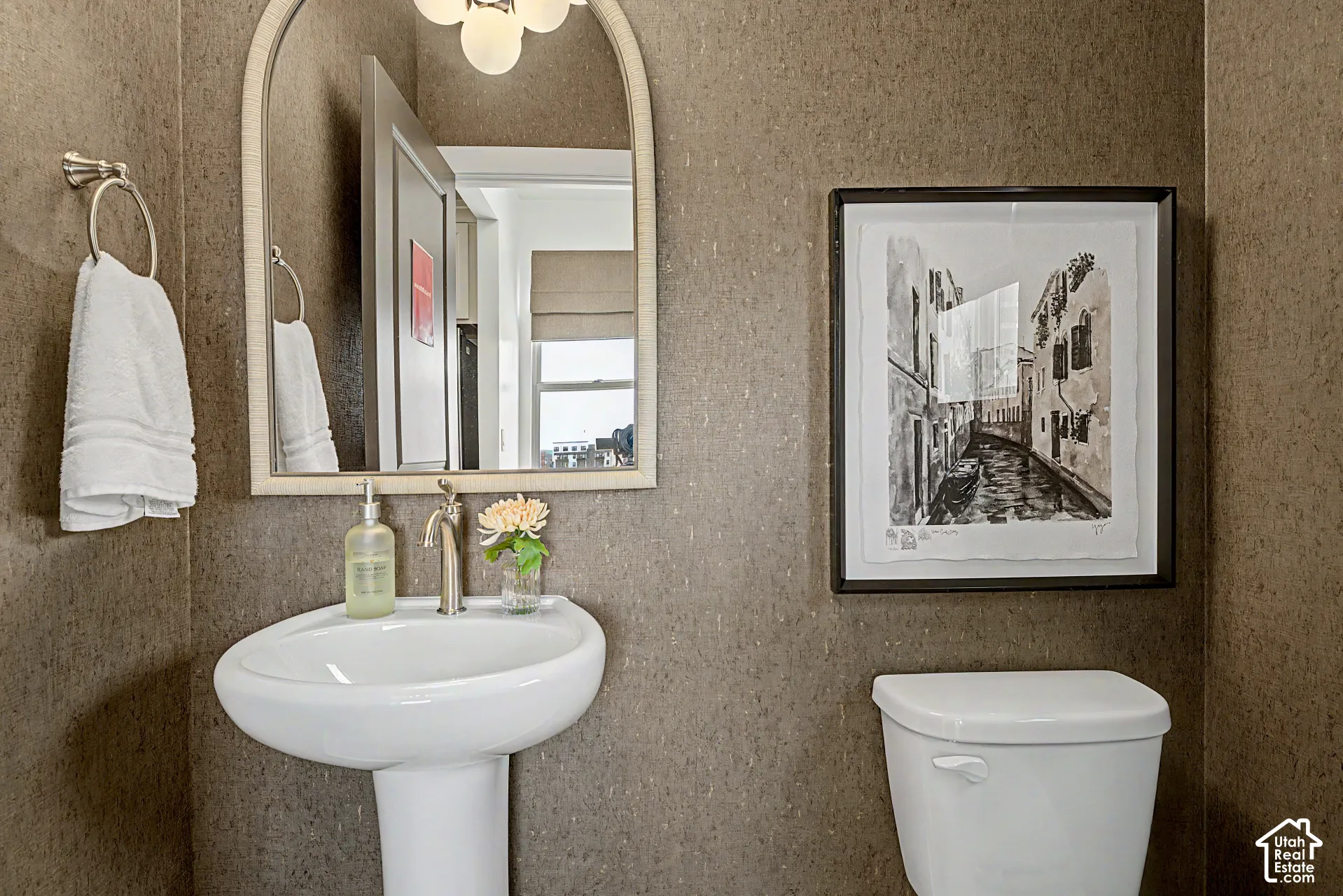 Pedestal sink with a brushed nickel faucet, arched mirror, and flush-mounted toilet
