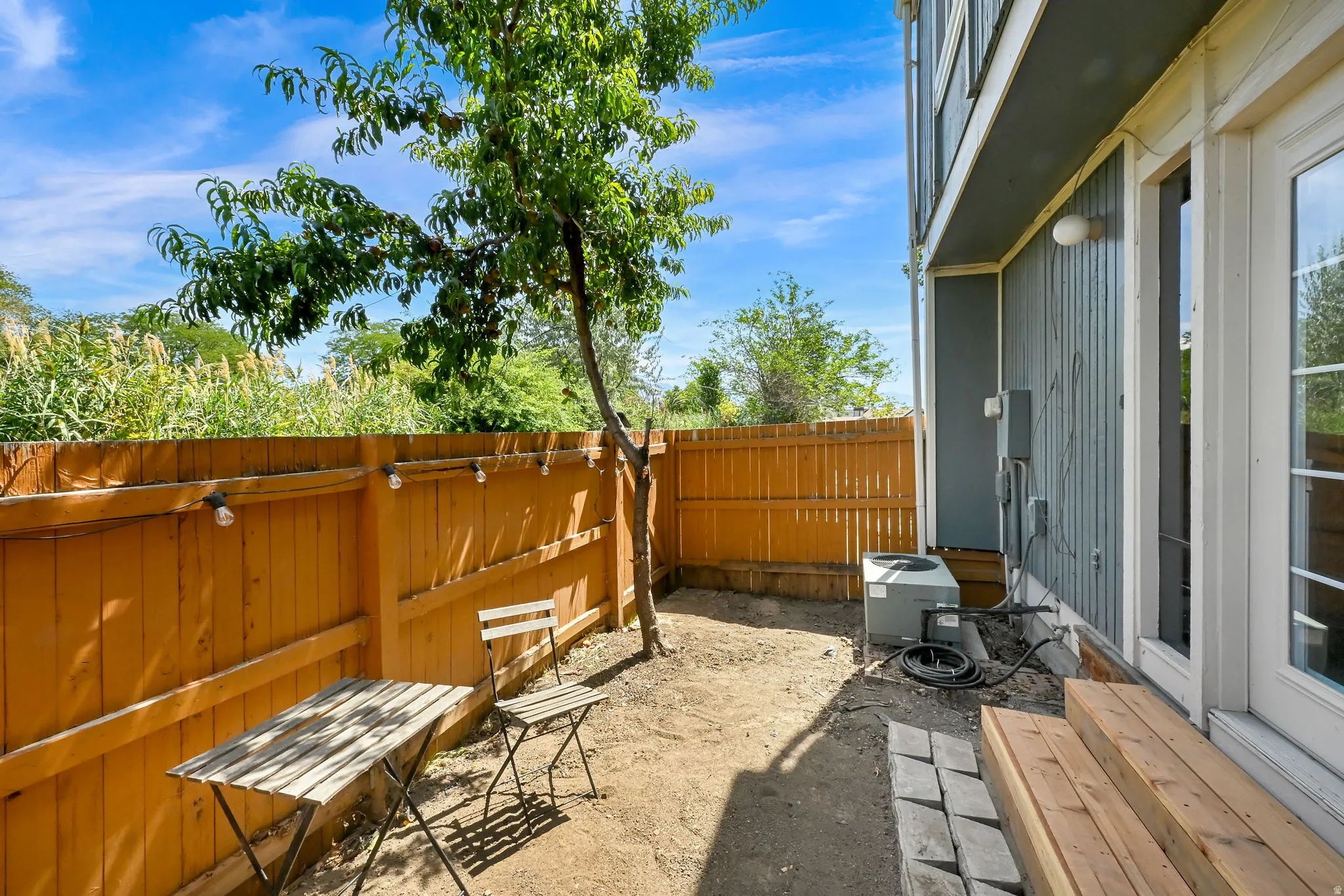 Fenced outdoor space featuring a mature tree, wood plank siding, and a multi-pane glass door