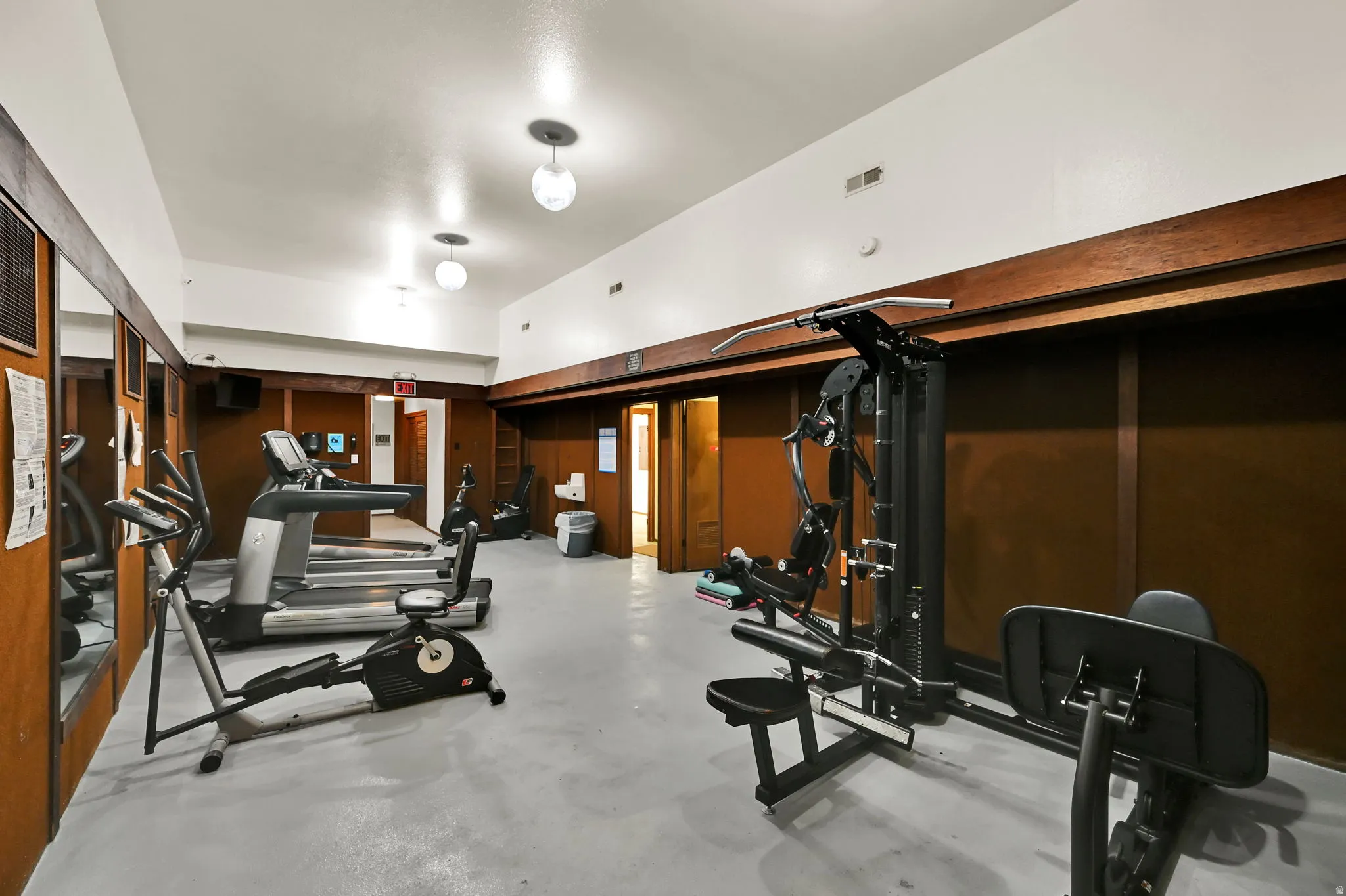 Spacious fitness area featuring wall-mounted mirrors, recessed lighting, and wood-paneled walls