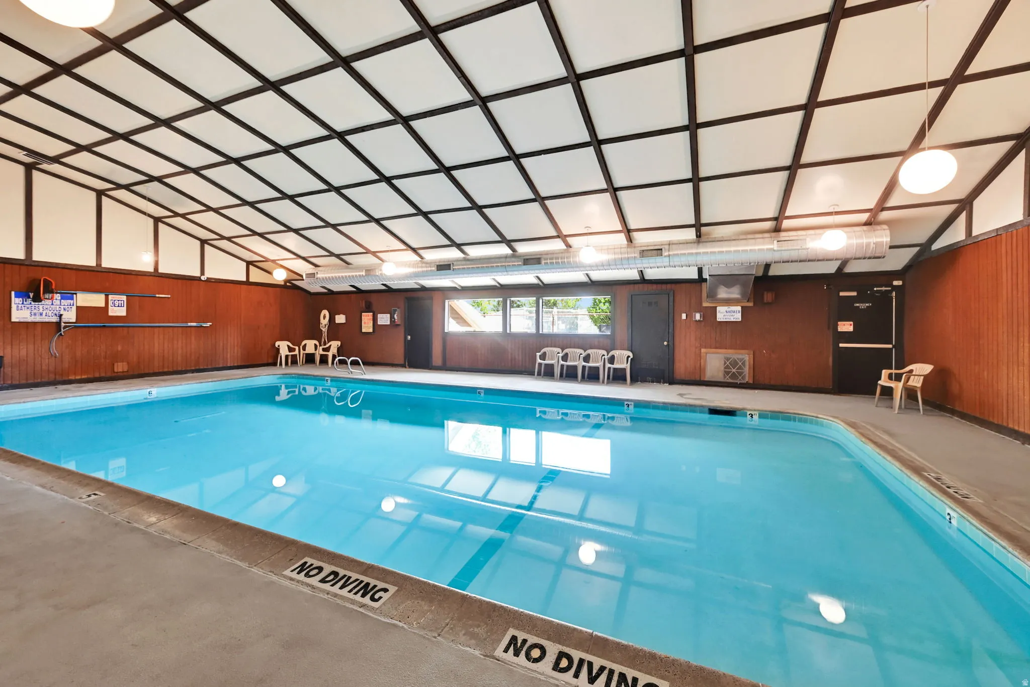 Indoor swimming pool with concrete decking, wood-paneled walls, and a vaulted grid ceiling with integrated lighting