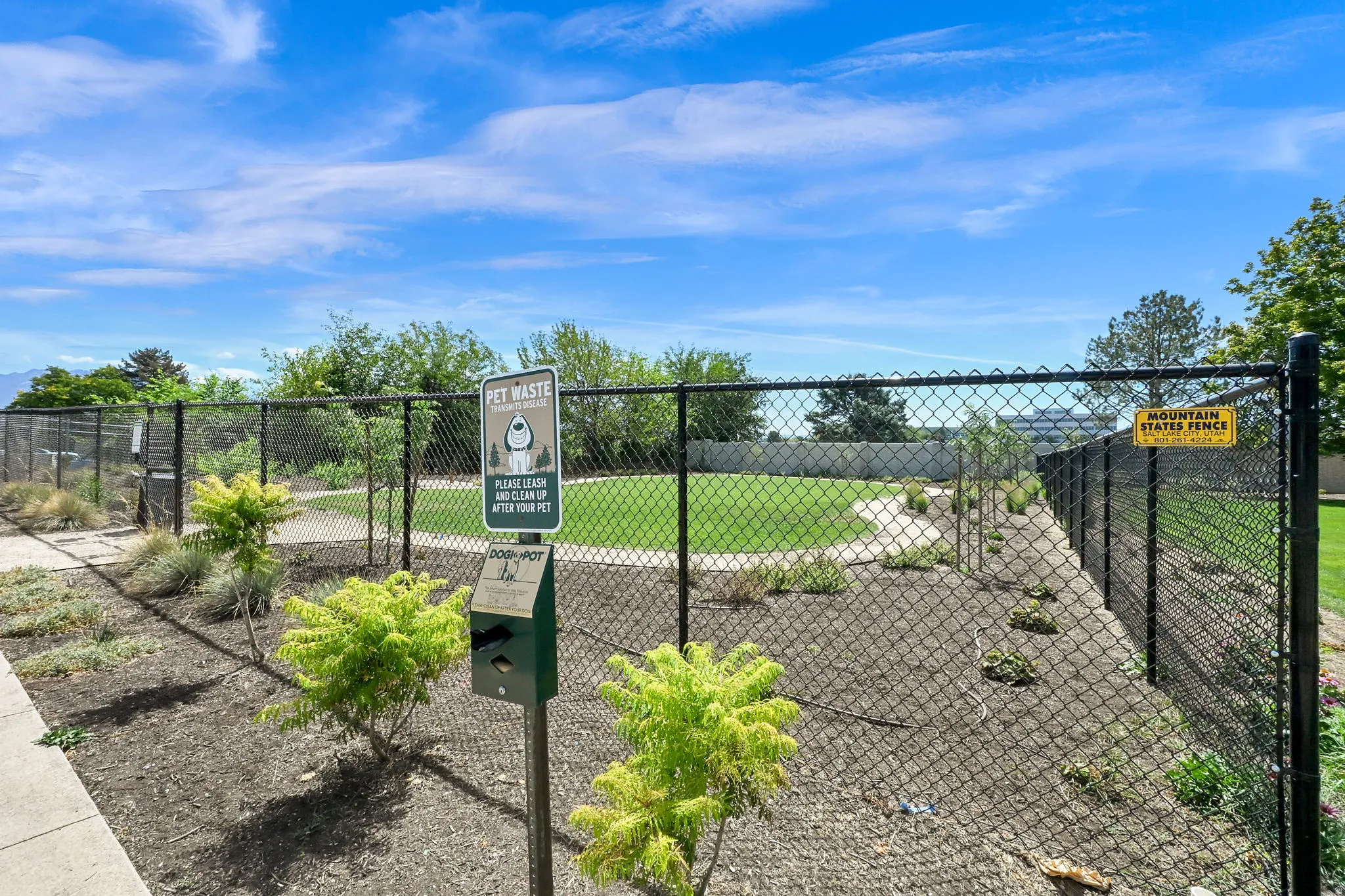 Dog park with a pet waste station, bordered by landscaped ground cover and mature trees
