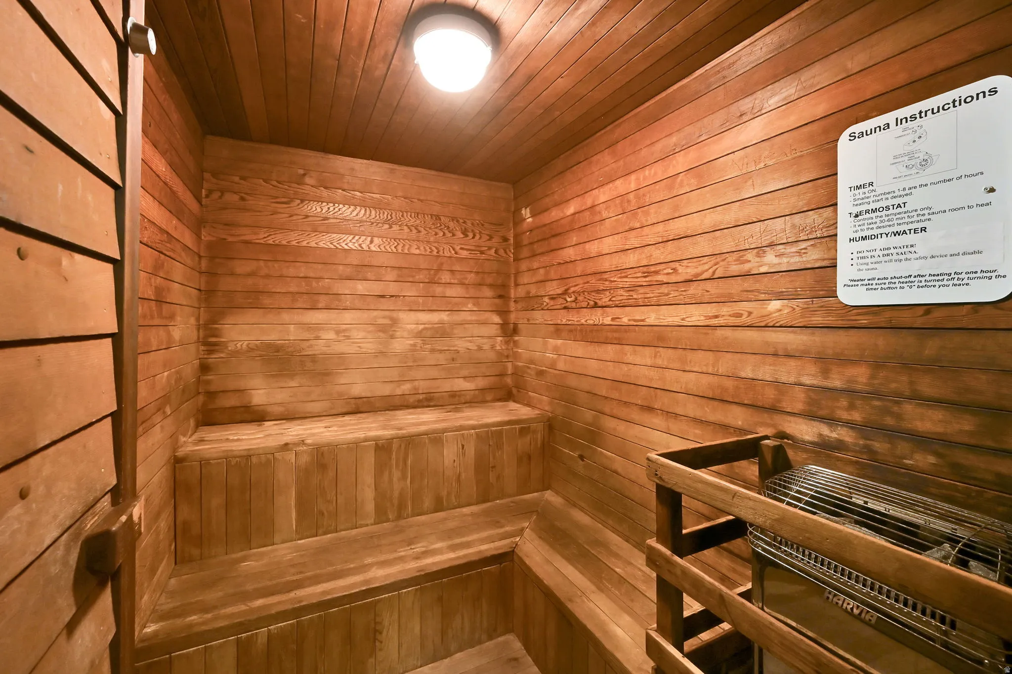 Wood-paneled sauna featuring built-in benches, a ceiling-mounted light fixture, and a sauna heating unit