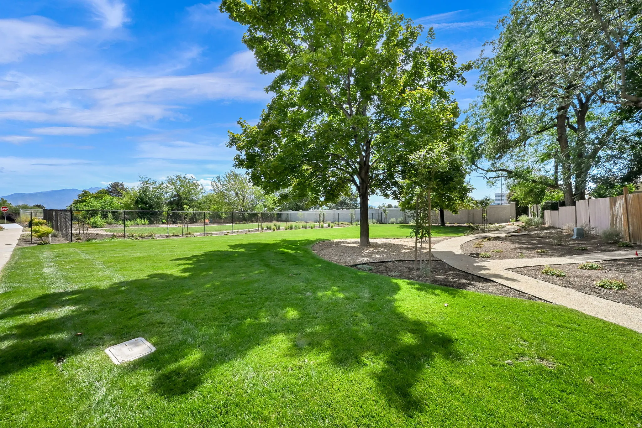 Expansive green lawn, mature trees, gravel pathways, perimeter fencing, and distant mountain backdrop