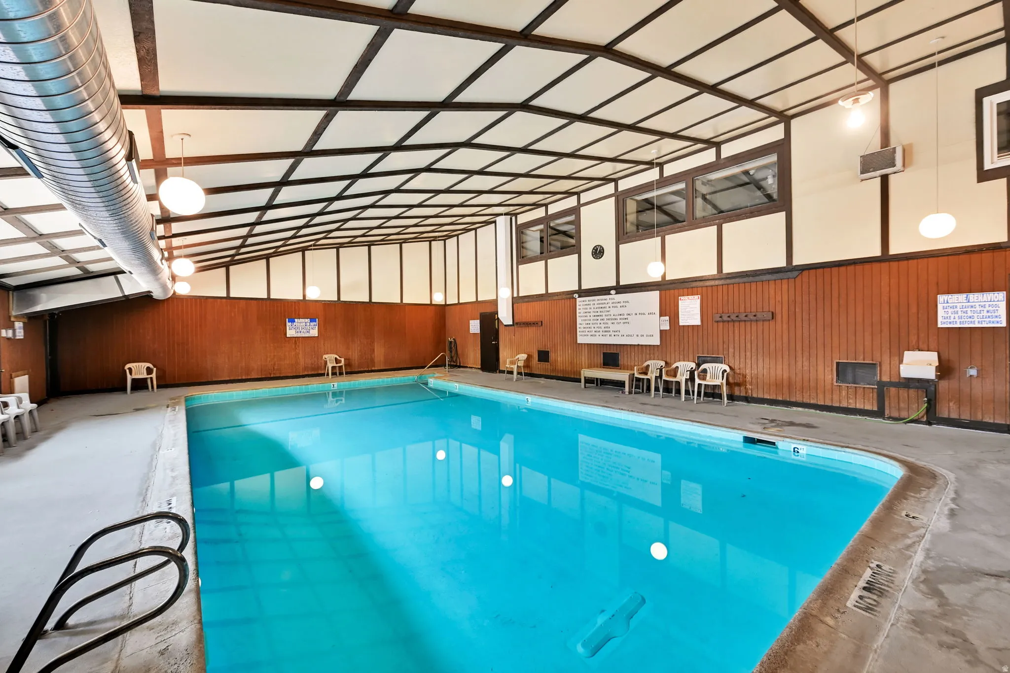 Indoor swimming pool with concrete decking, wood-paneled walls, and a beamed ceiling